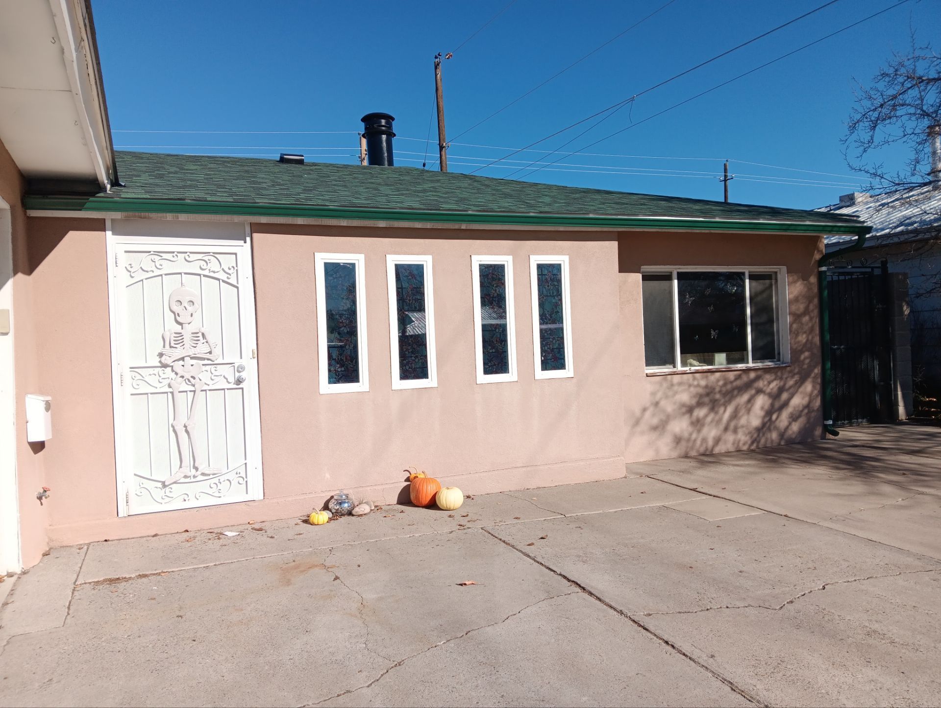 Tan building with green roof, white security door, small windows, and pumpkins on the concrete.