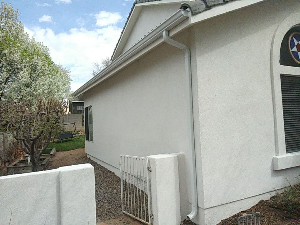 White stucco house with gutter and small gate in front, with a tree in the background.