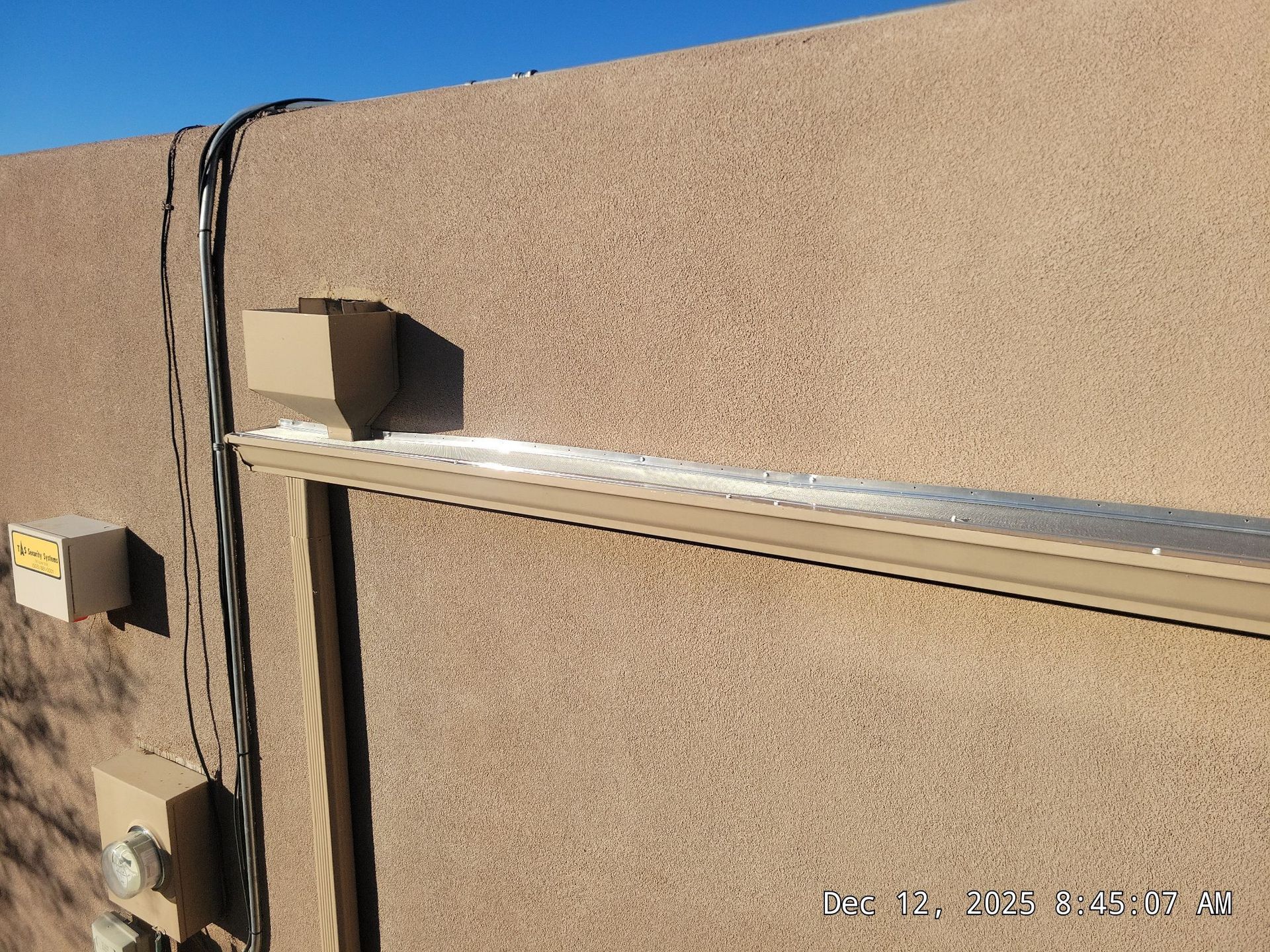 Tan stucco wall with electrical boxes and wires, and a metal awning.