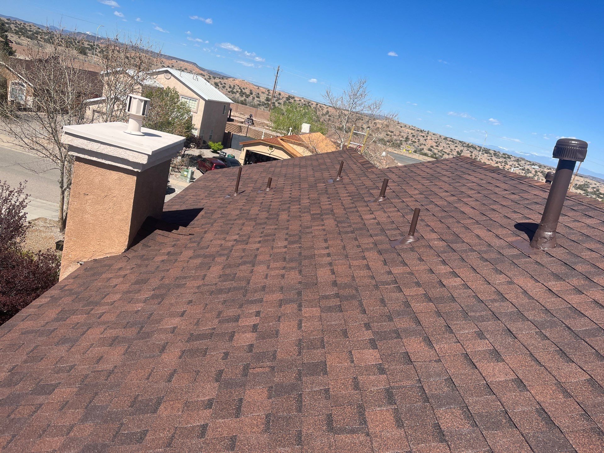A brown shingle roof with a chimney and vents under a blue sky.