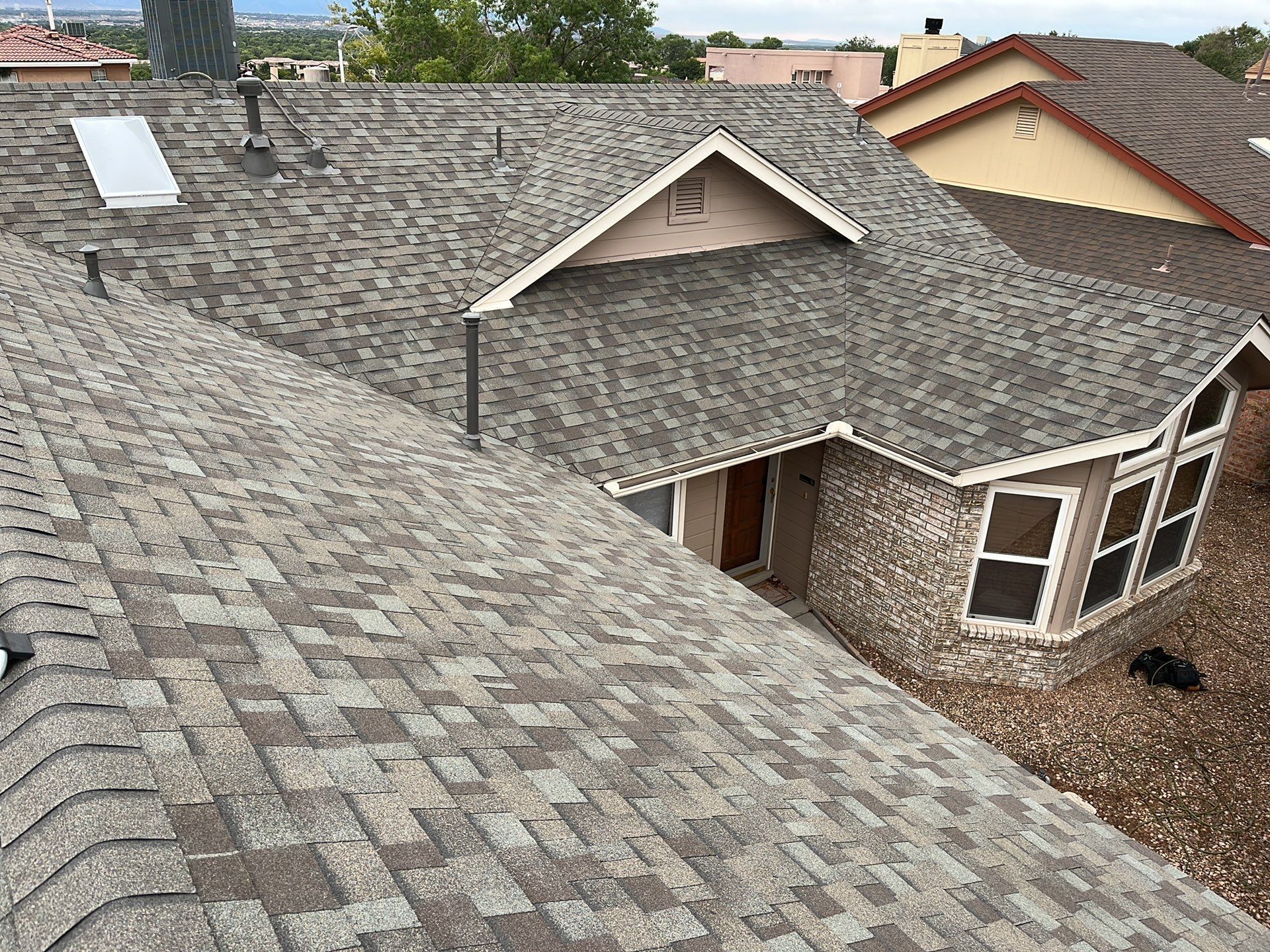 Overhead view of a house with brown shingle roof. Sunlit setting.