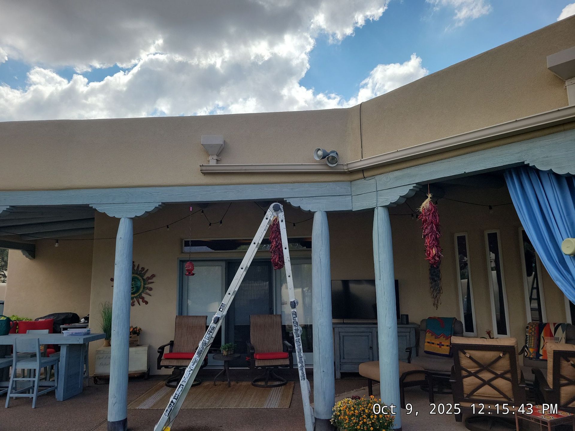 A ladder leans against a building's pale turquoise colonnade. The sky is cloudy and the building is tan.