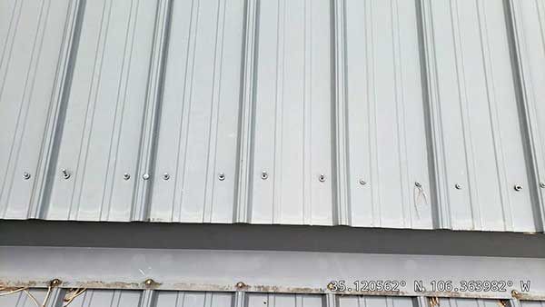 Gray metal corrugated siding on a building with visible fasteners along the bottom edge.