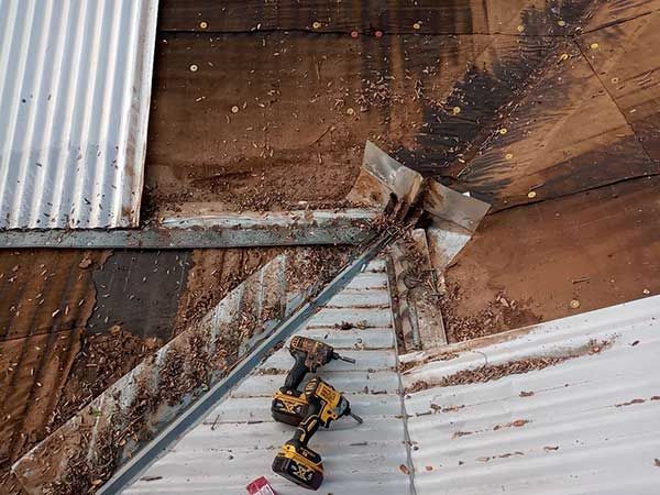 Roof repair: metal and wood roofing with tools, debris, and torn section.