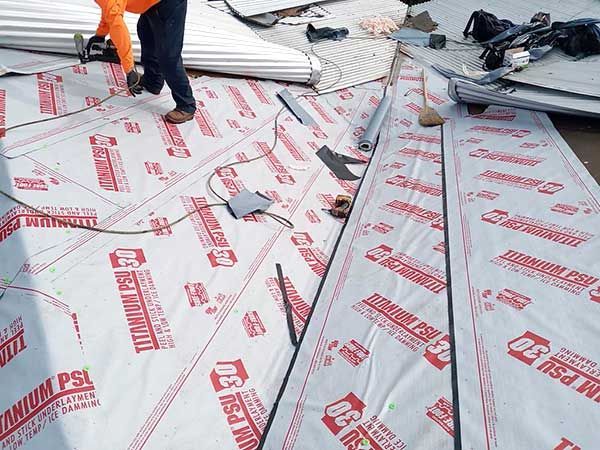 Roofer installing roofing underlayment labeled 