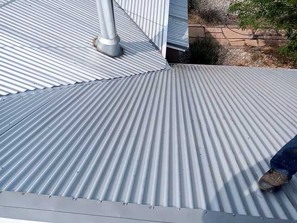 Corrugated metal roof with a chimney, a gutter, and a person's leg and foot visible.