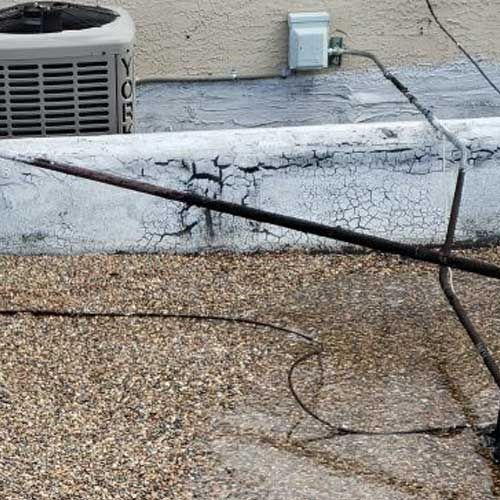 AC unit and electrical outlet on a weathered roof, with cracked paint and exposed wires.