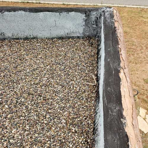 Flat roof with gravel, showing edge with sealant and concrete wall.