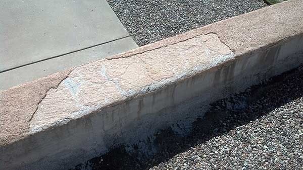 Damaged concrete wall, showing flaking and water stains.