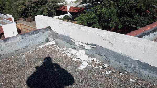 View of a flat roof with peeling white sealant along the edge.