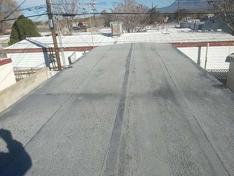 Flat, gray rooftop with a dark stripe down the center and distant buildings, power lines, and a mountain visible.