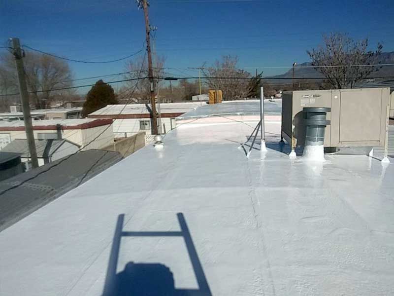 White roof with equipment, ladder shadow, telephone poles, and clear blue sky.