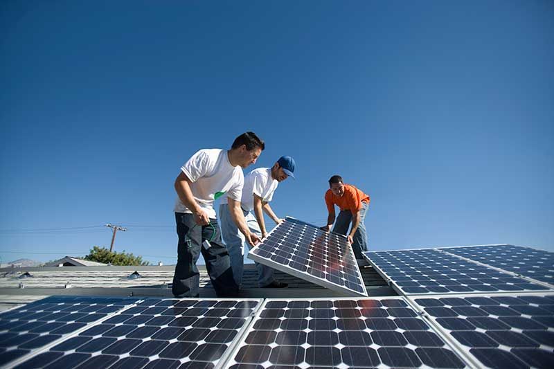 Three workers installing solar panels on a rooftop under a blue sky.