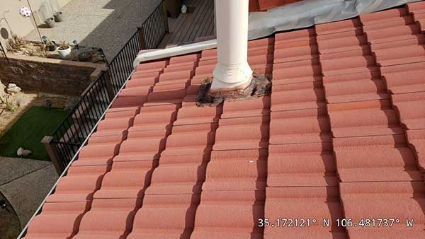 Red tile roof with white pipe and dark staining around base.