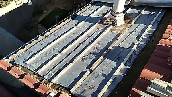 Rooftop with wooden planks, a white pipe, and red tile roof edges. Sunlight illuminates the scene.
