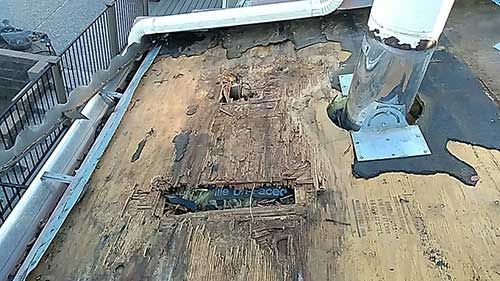 Damaged rooftop with visible rot, a metal vent, and a gutter, likely needing repair.