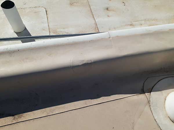 A close-up of a flat, light-colored roof with a raised edge and a vent pipe.