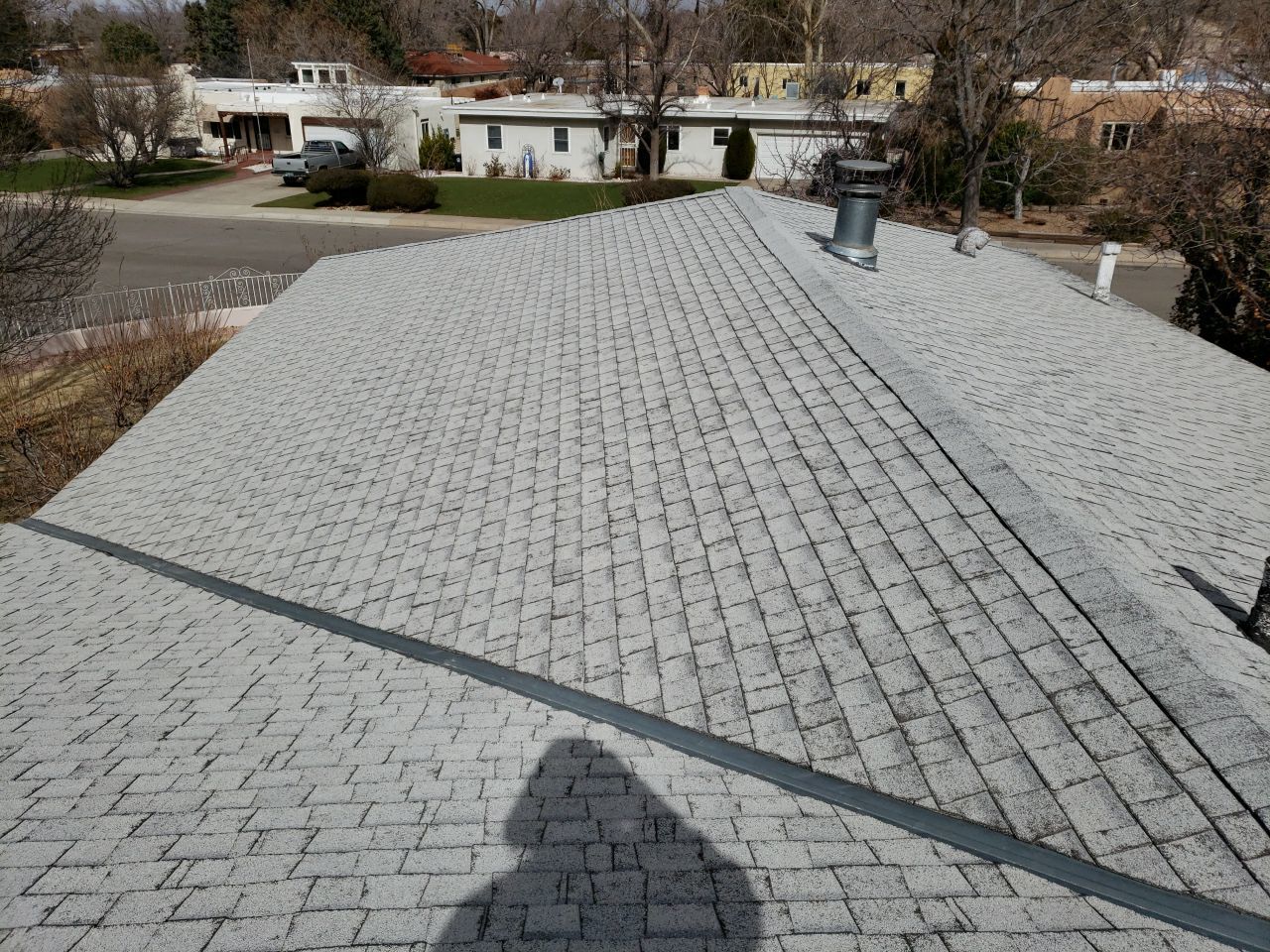 Gray asphalt shingle roof on a residential building, with a vent pipe and flashing visible.