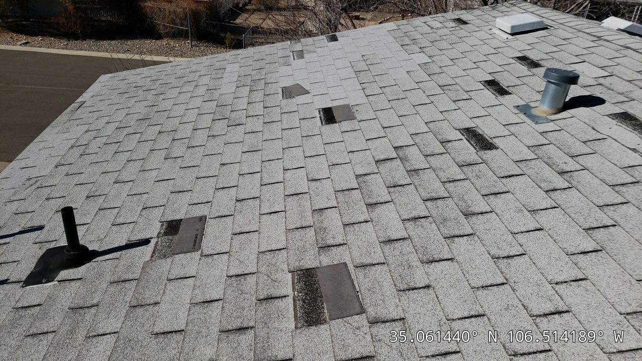 Damaged asphalt shingle roof, gray with missing and discolored shingles, various vents.
