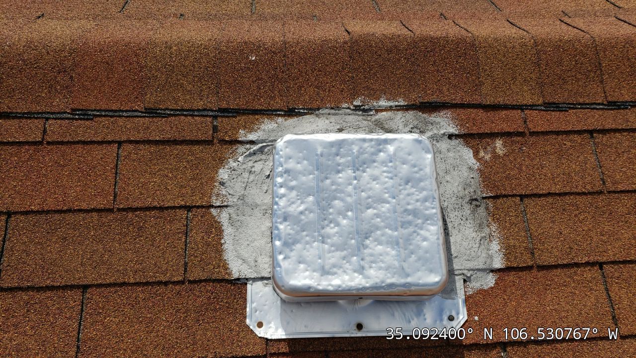 Silver roof vent on brown asphalt shingles, sealed with white sealant.