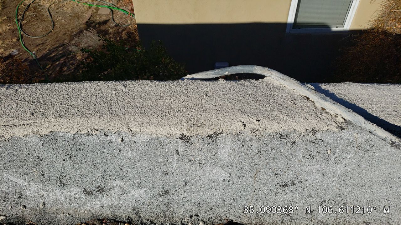 Gray cement wall with a white edge and a hose extending from the upper side.