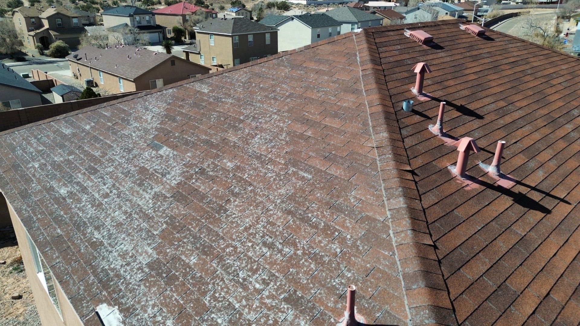 Brown shingled roof with white debris, possibly hail damage, in residential area.