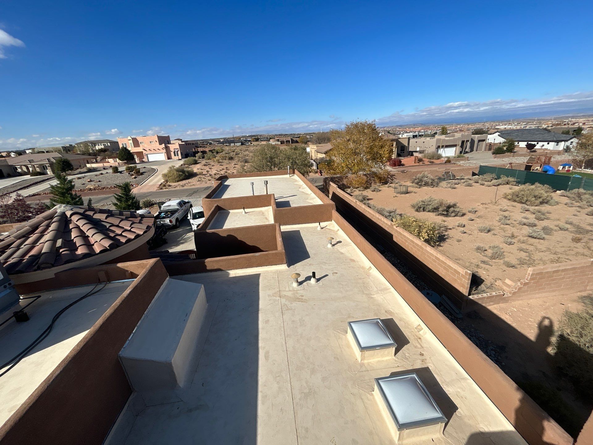 Flat rooftops with brown trim; suburban houses and desert landscape under a clear blue sky.