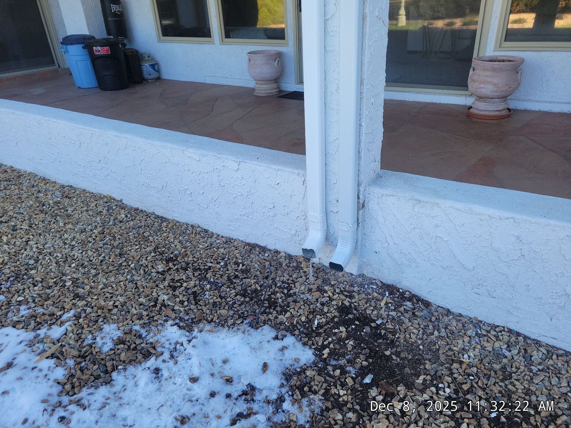 White stucco building with gravel ground, snow patch, and a downspout.