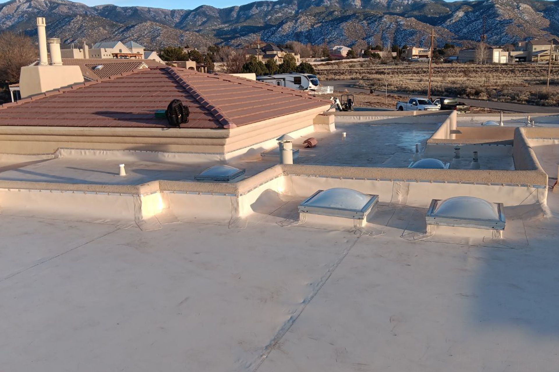 Rooftop view of buildings with a tile roof and flat roofs with skylights, against a mountain backdrop.