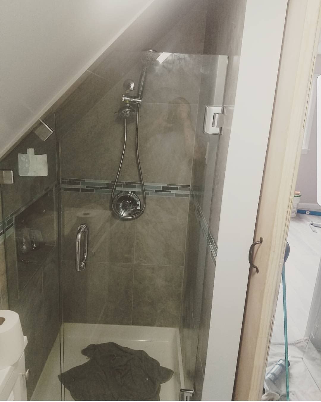 A bathroom with a walk in shower under a slanted ceiling