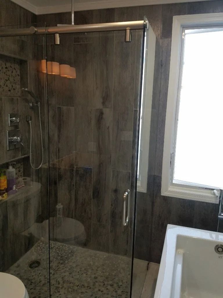 A bathroom with a sliding glass shower door , toilet , tub and window.