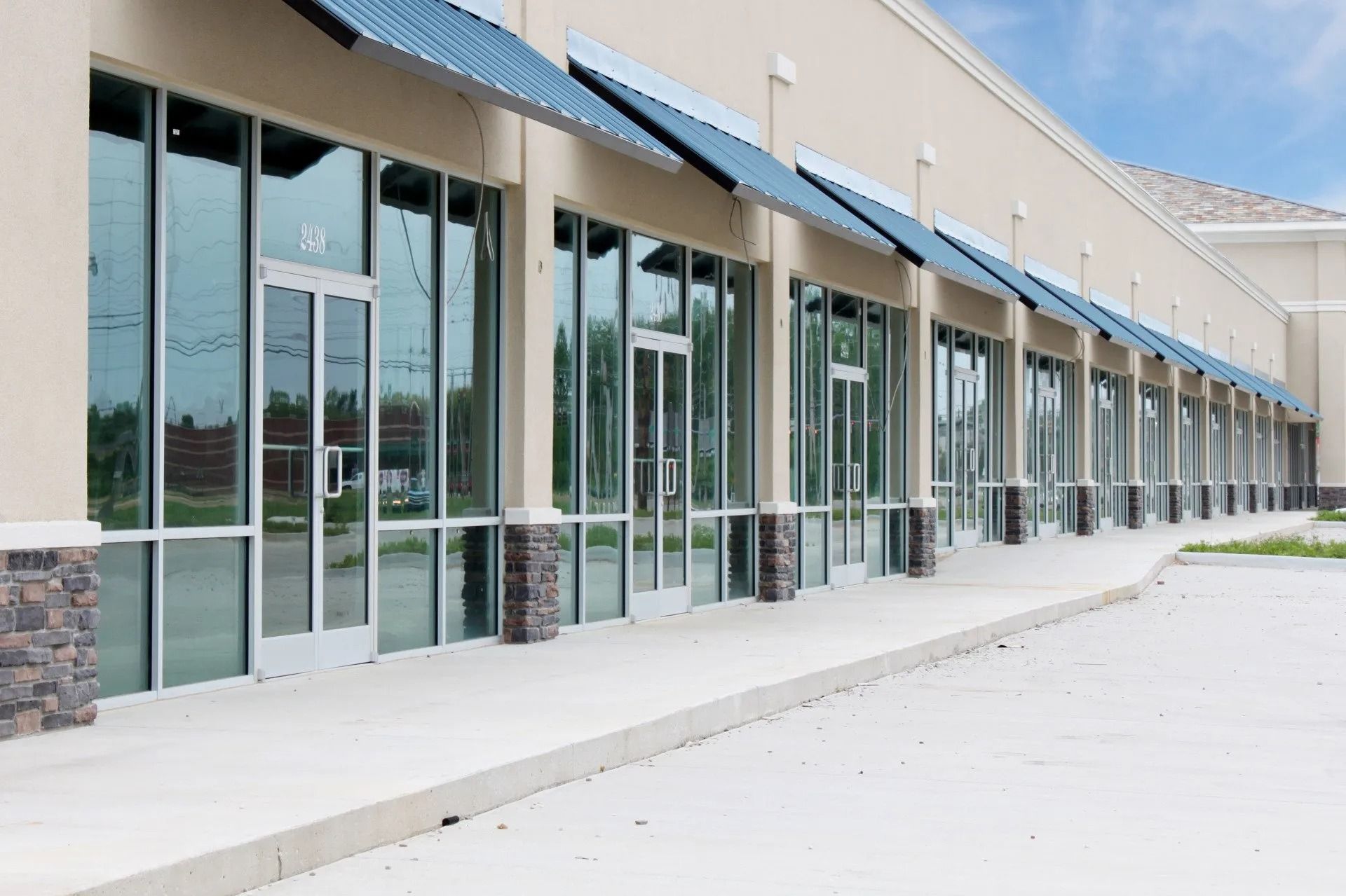 Row of commercial storefronts with large glass windows and blue awnings, on a sunny day.