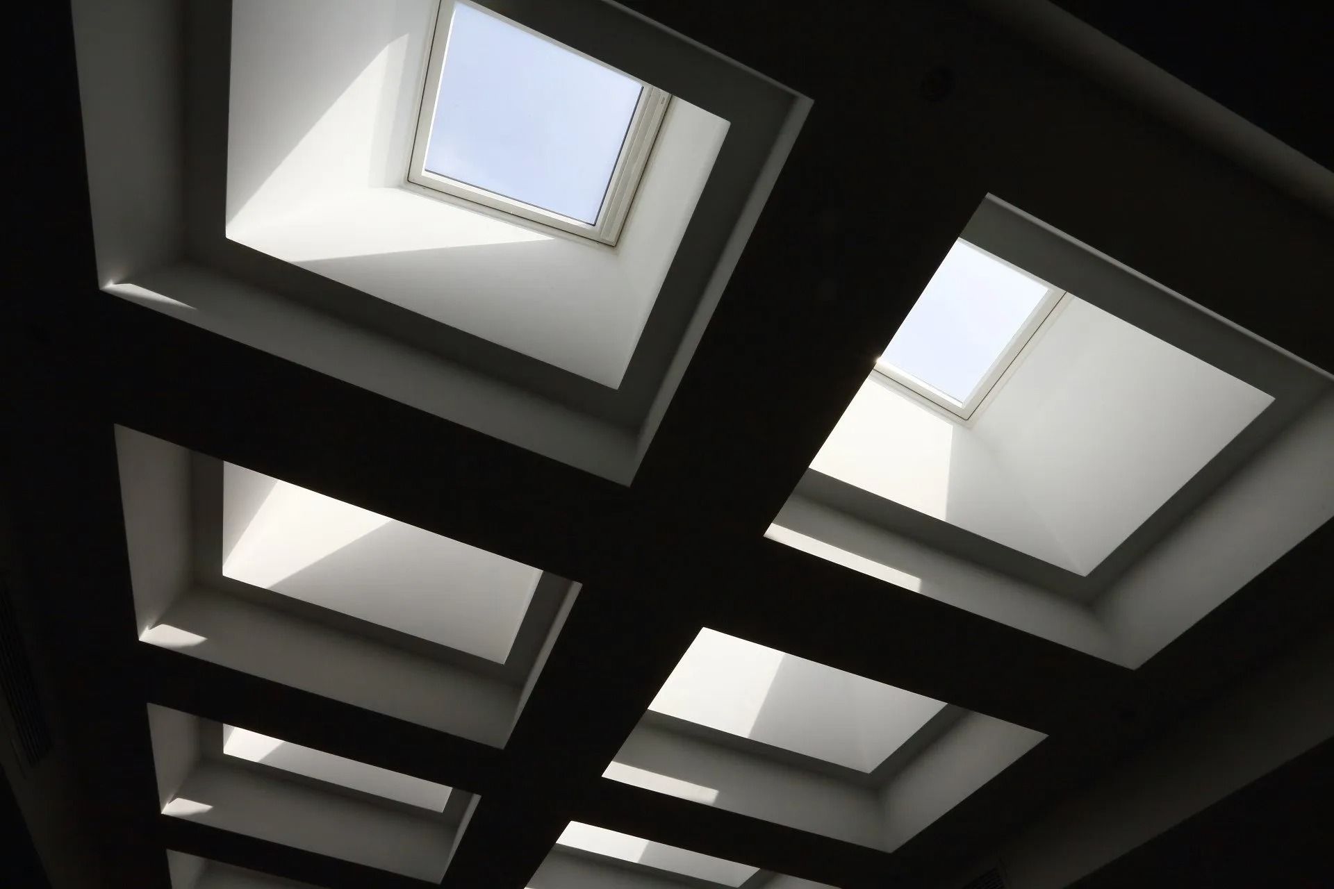 Skylights in a ceiling let in bright sunlight, creating contrasting light and shadow patterns.