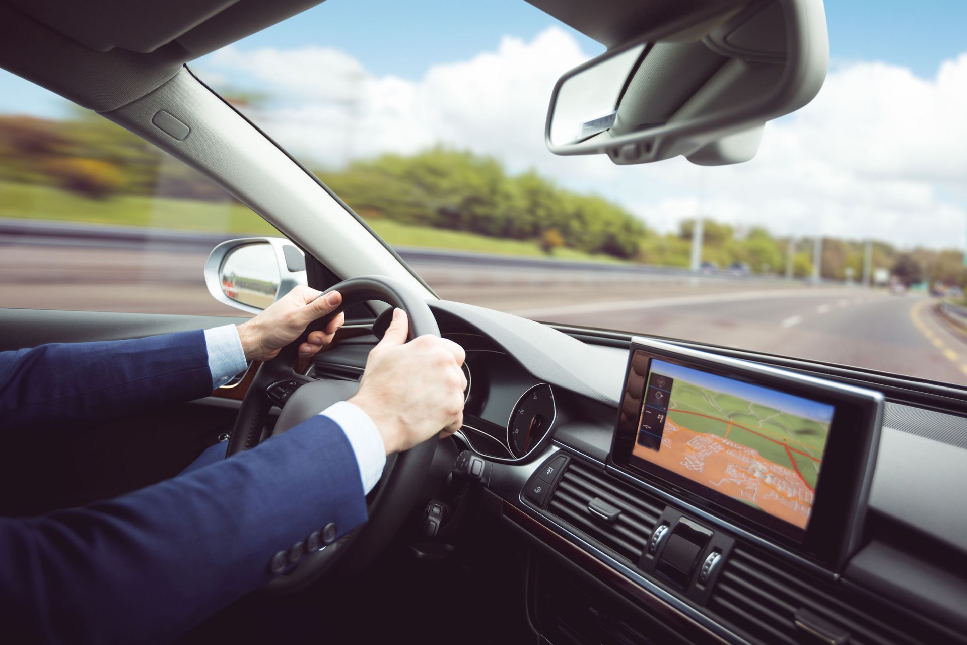 Driver holding steering wheel in a car, with dashboard navigation screen showing a road map.