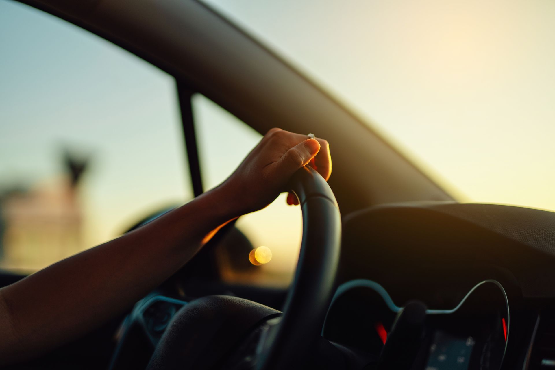 Hand on steering wheel in a car at sunset, with warm light streaming through the window.
