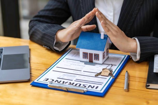 Hands framing a small model house on an insurance application form at a desk