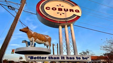 Coburg roadside sign with a cow statue and slogan “Better than it has to be”