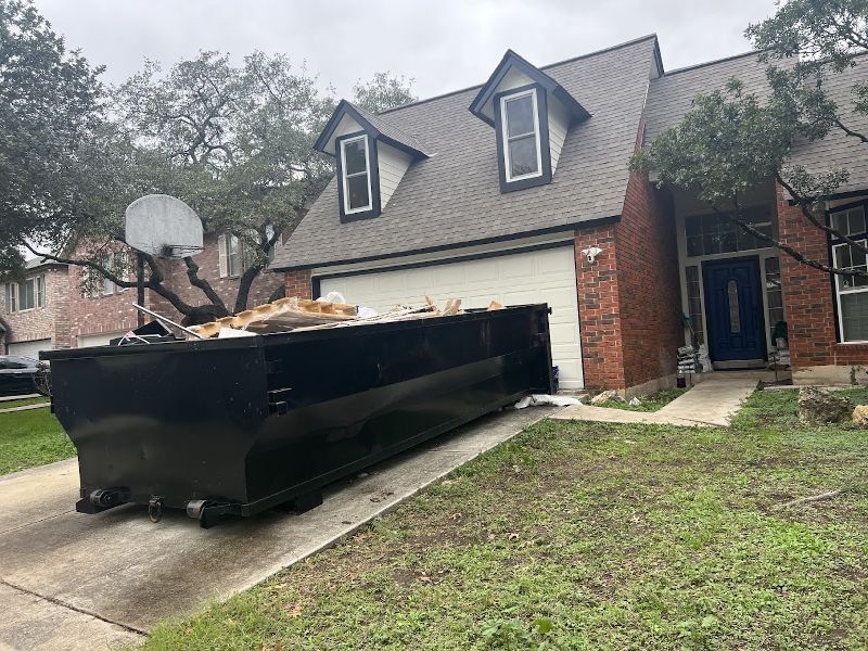 A large black dumpster is parked in front of a brick house.