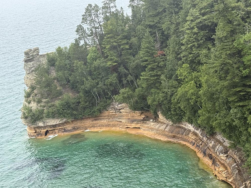 Cliffside covered in green trees overlooks turquoise water.