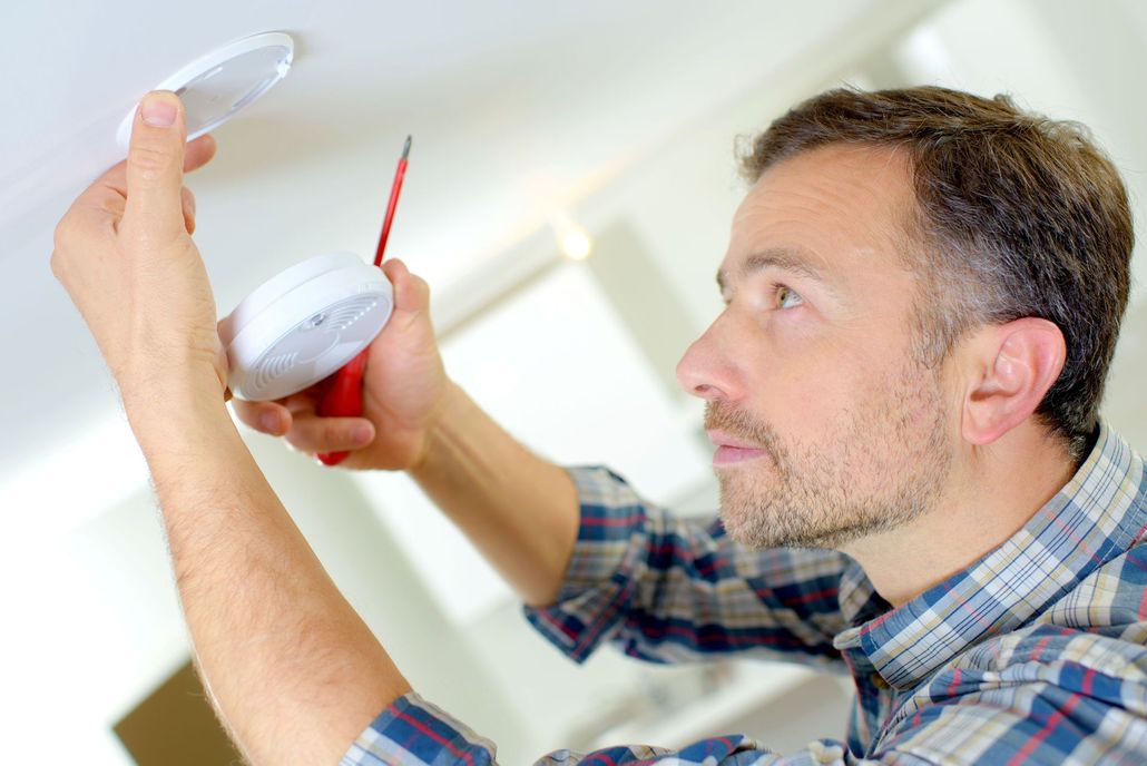 Technician using a power drill to install a device on an exterior wall under a roof overhang