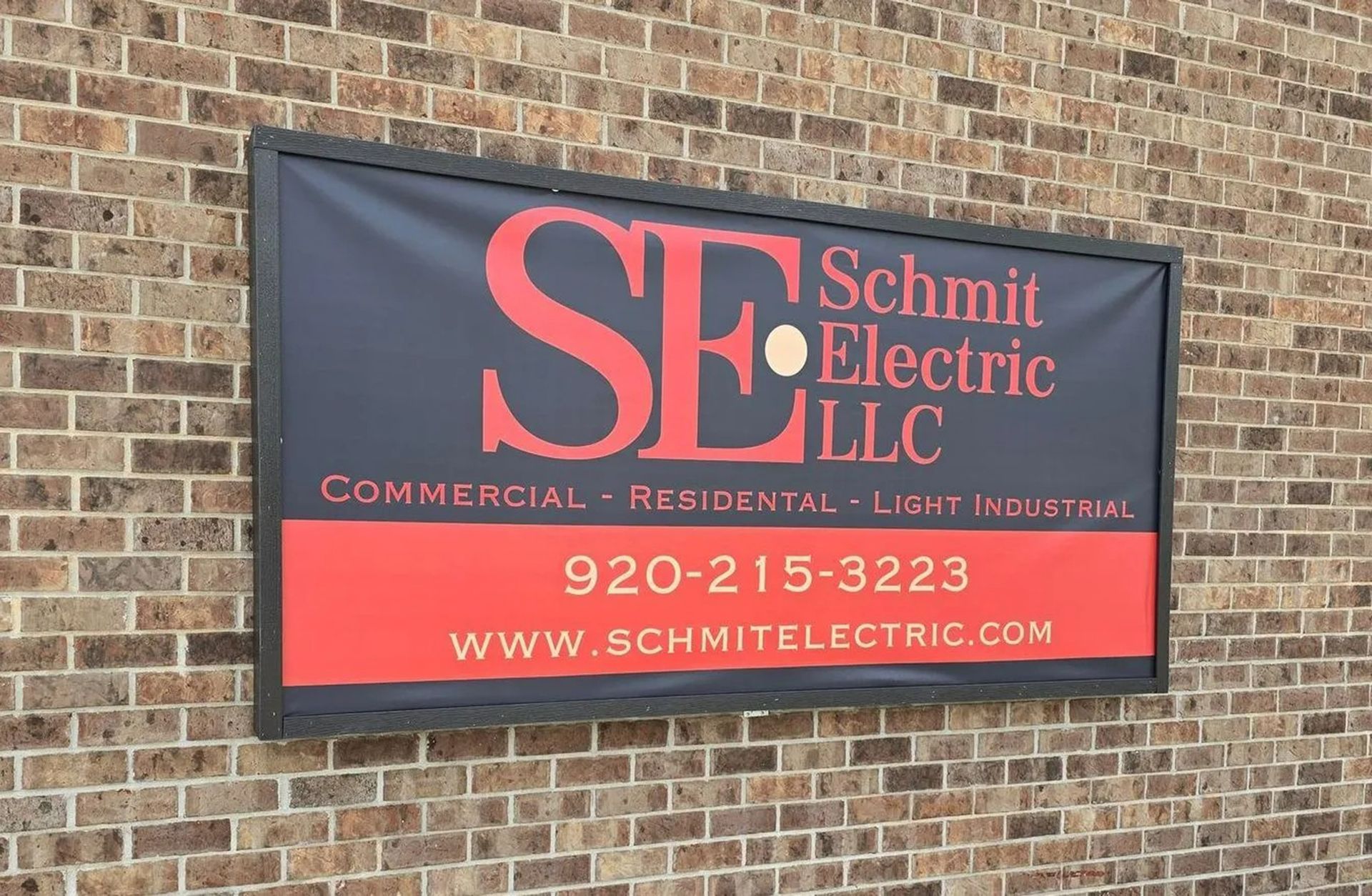Schmit Electric LLC sign on brick wall, black and red banner with phone number and website
