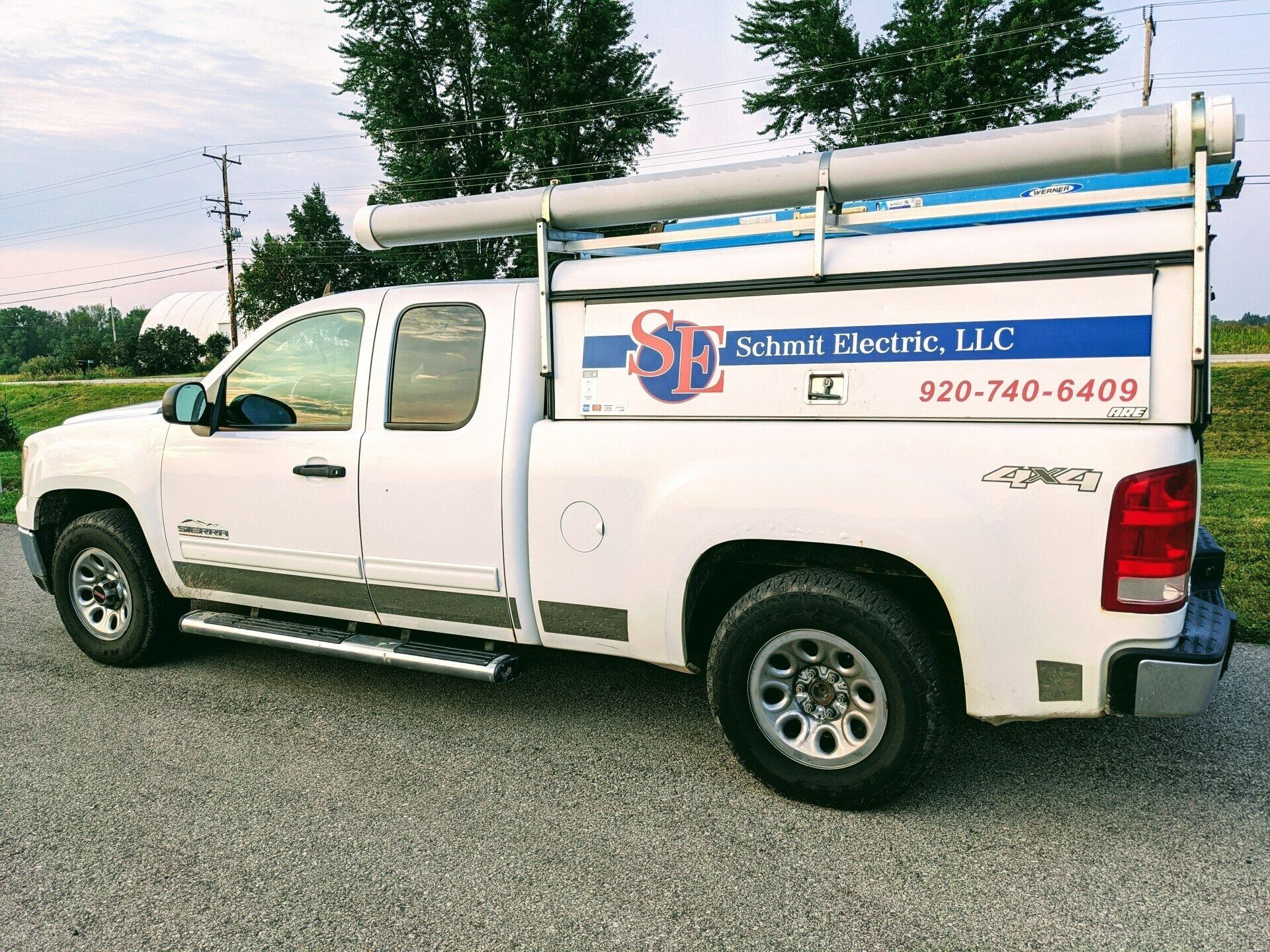 White Schaefer Electric LLC service truck parked on gravel, with ladder rack and company logo on the side.