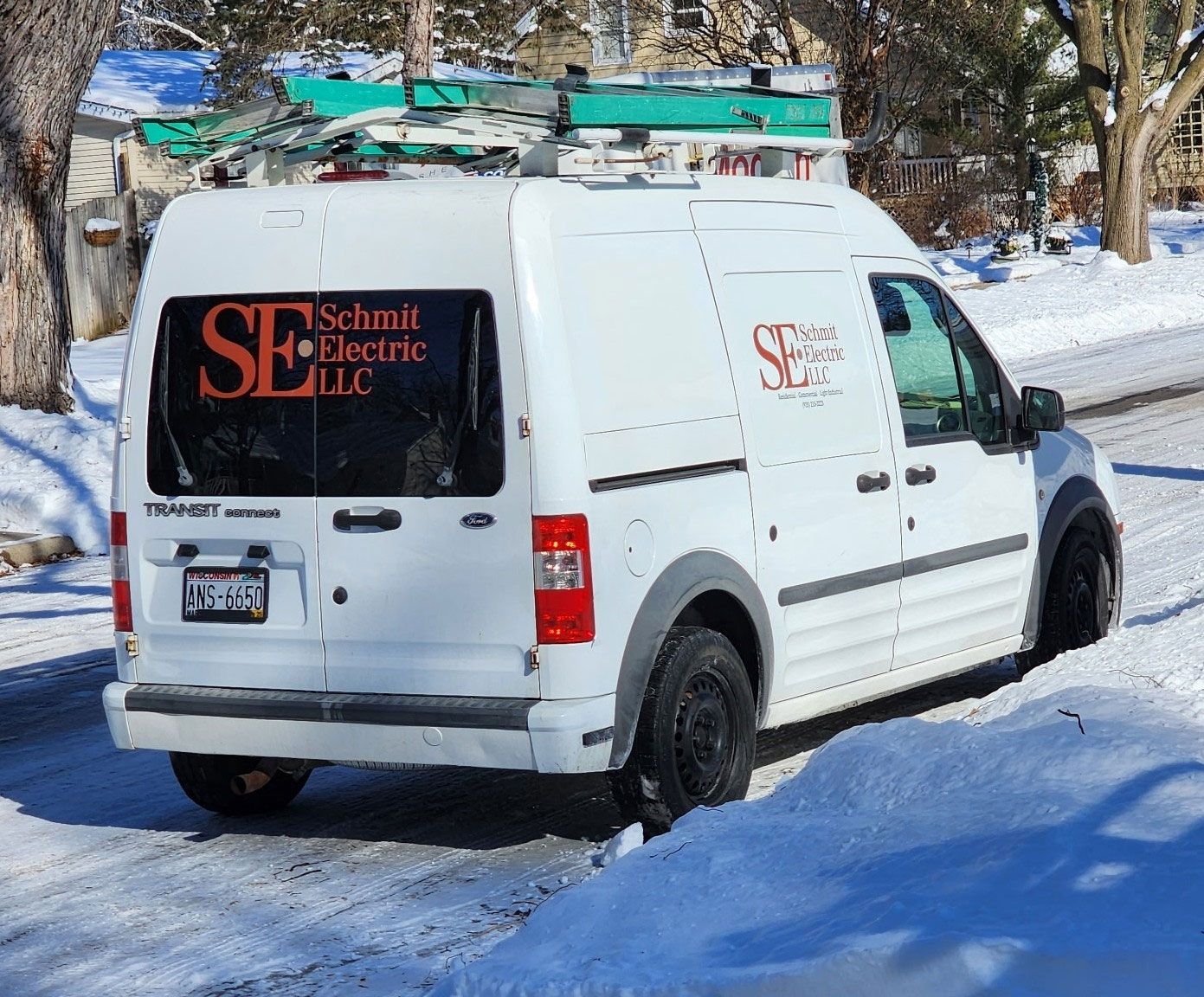 White service van with ladder on roof parked in a snowy driveway, bearing a red-and-black logo.