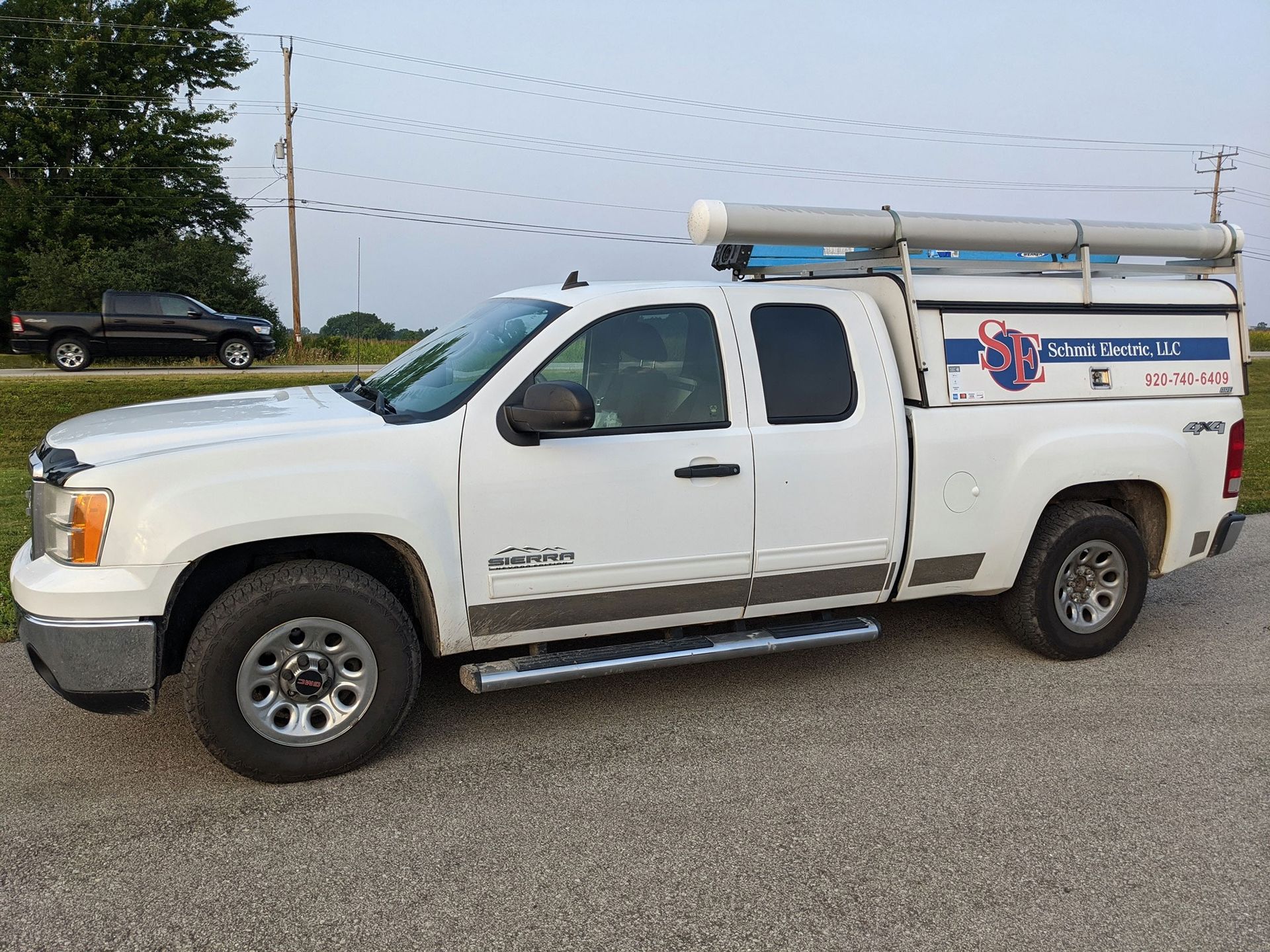 White utility pickup truck with a ladder rack parked on a roadside in an industrial area