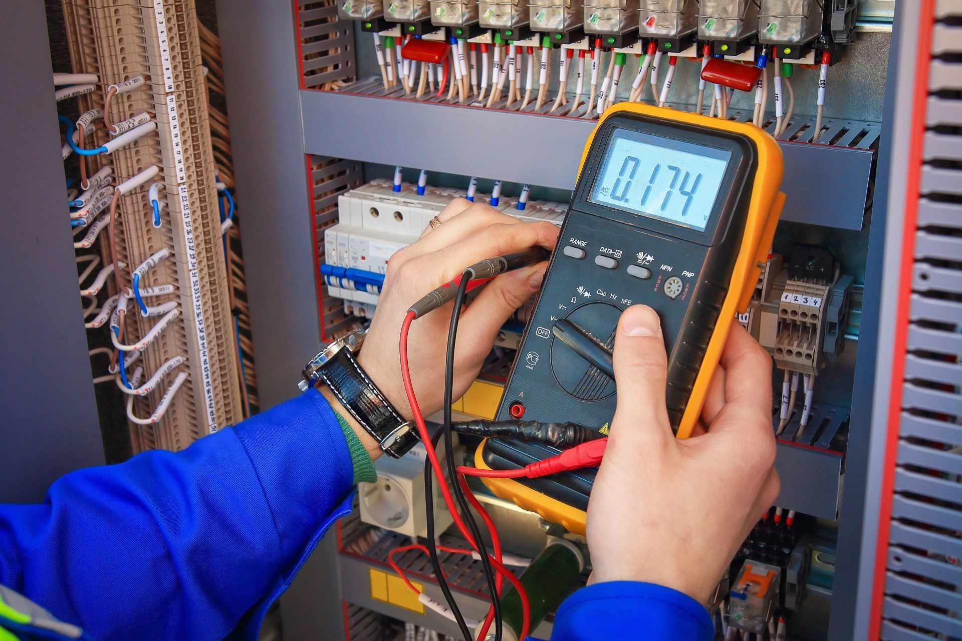 Technician using a digital multimeter to test wiring in an electrical control panel