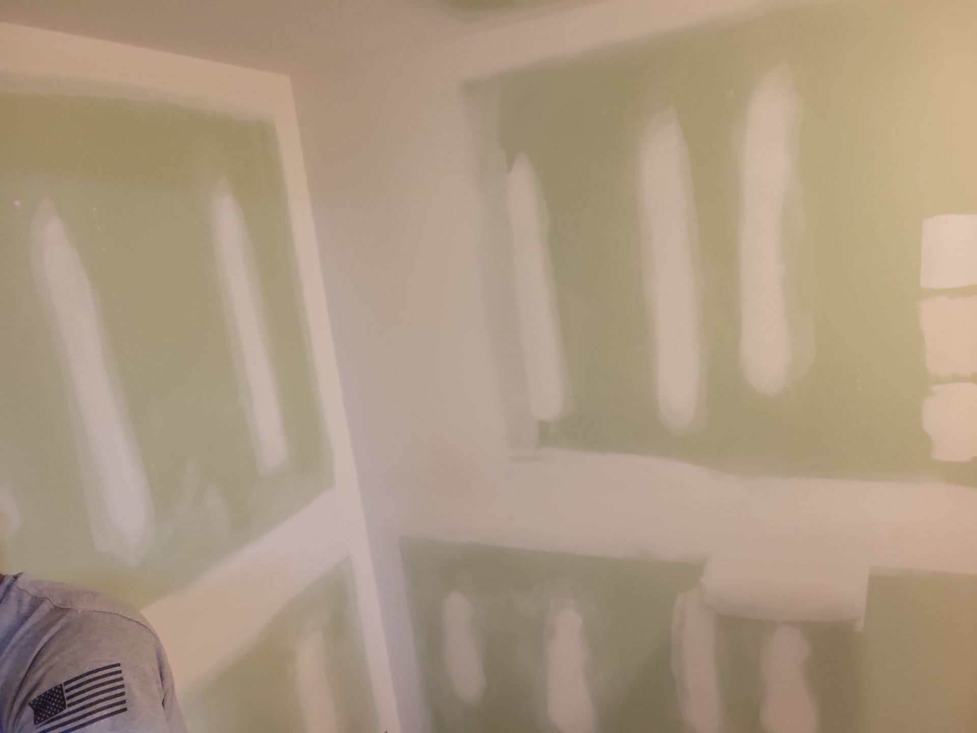 Partially painted room with green drywall and white joint compound patches under renovation.
