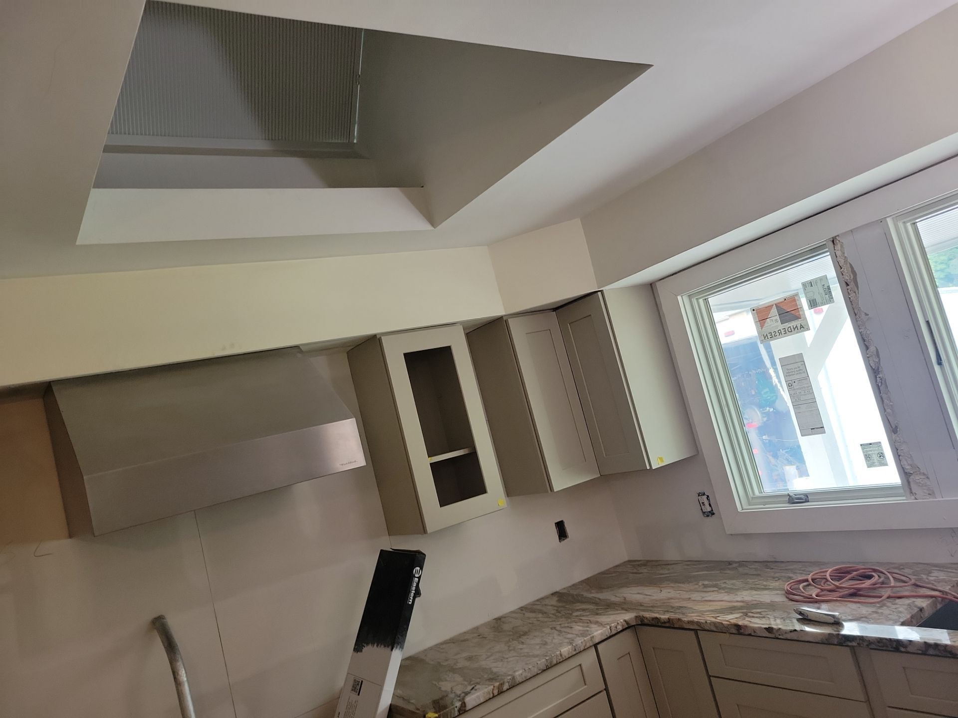Kitchen interior with white cabinets, granite countertop, and large window under renovation.