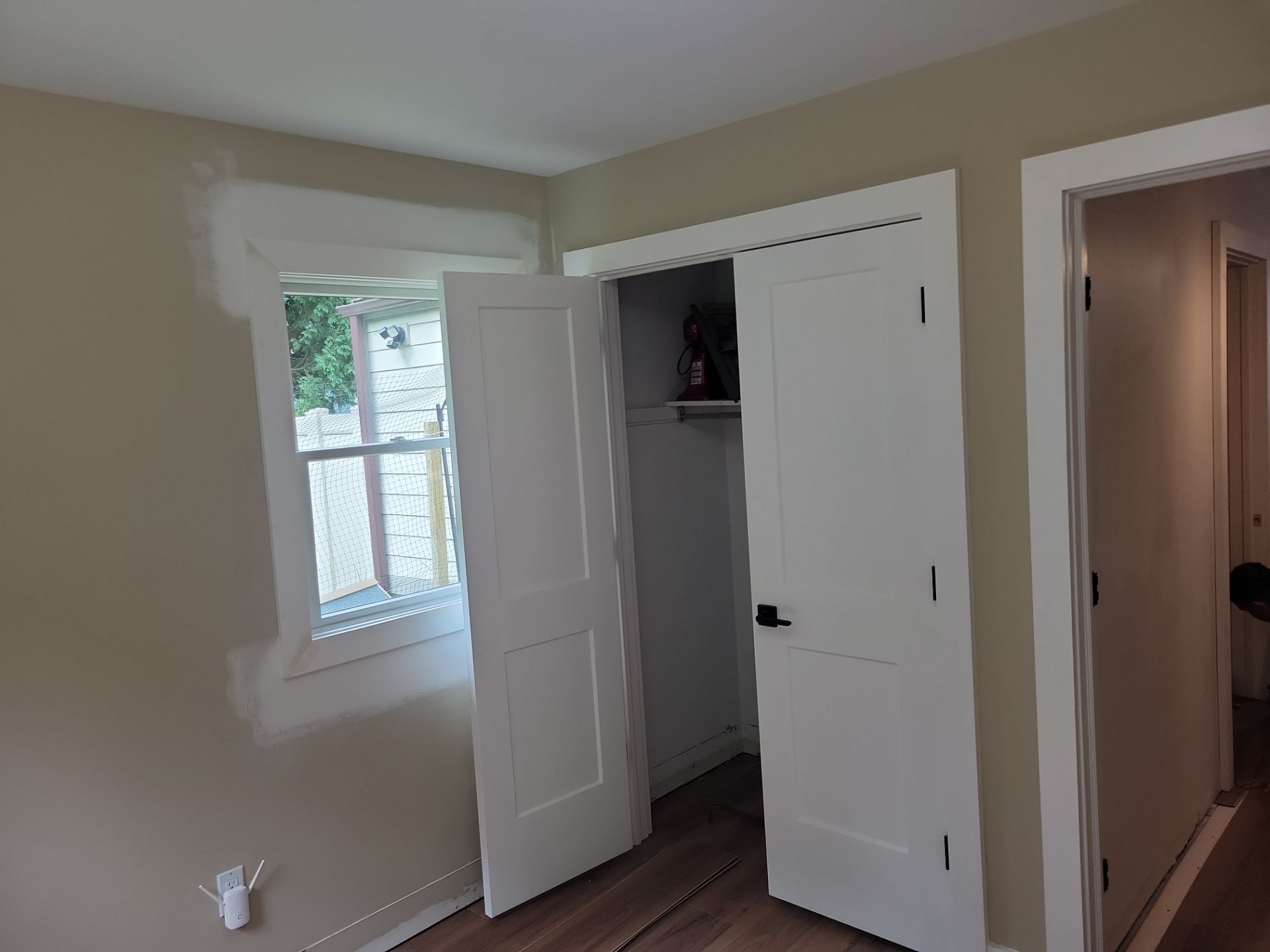 Empty beige bedroom with open closet doors and a window beside a hallway doorway.