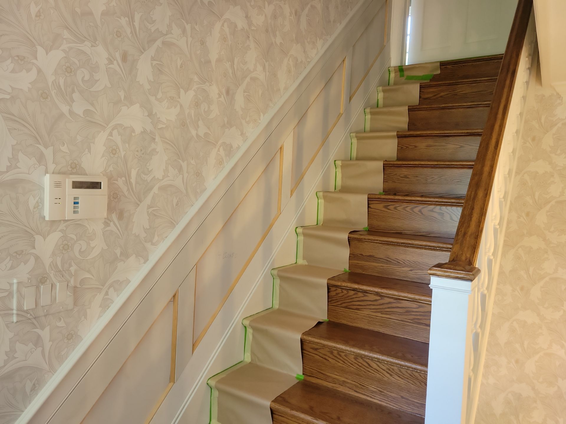 Staircase with wooden steps and pale wallpaper in a narrow indoor hallway.