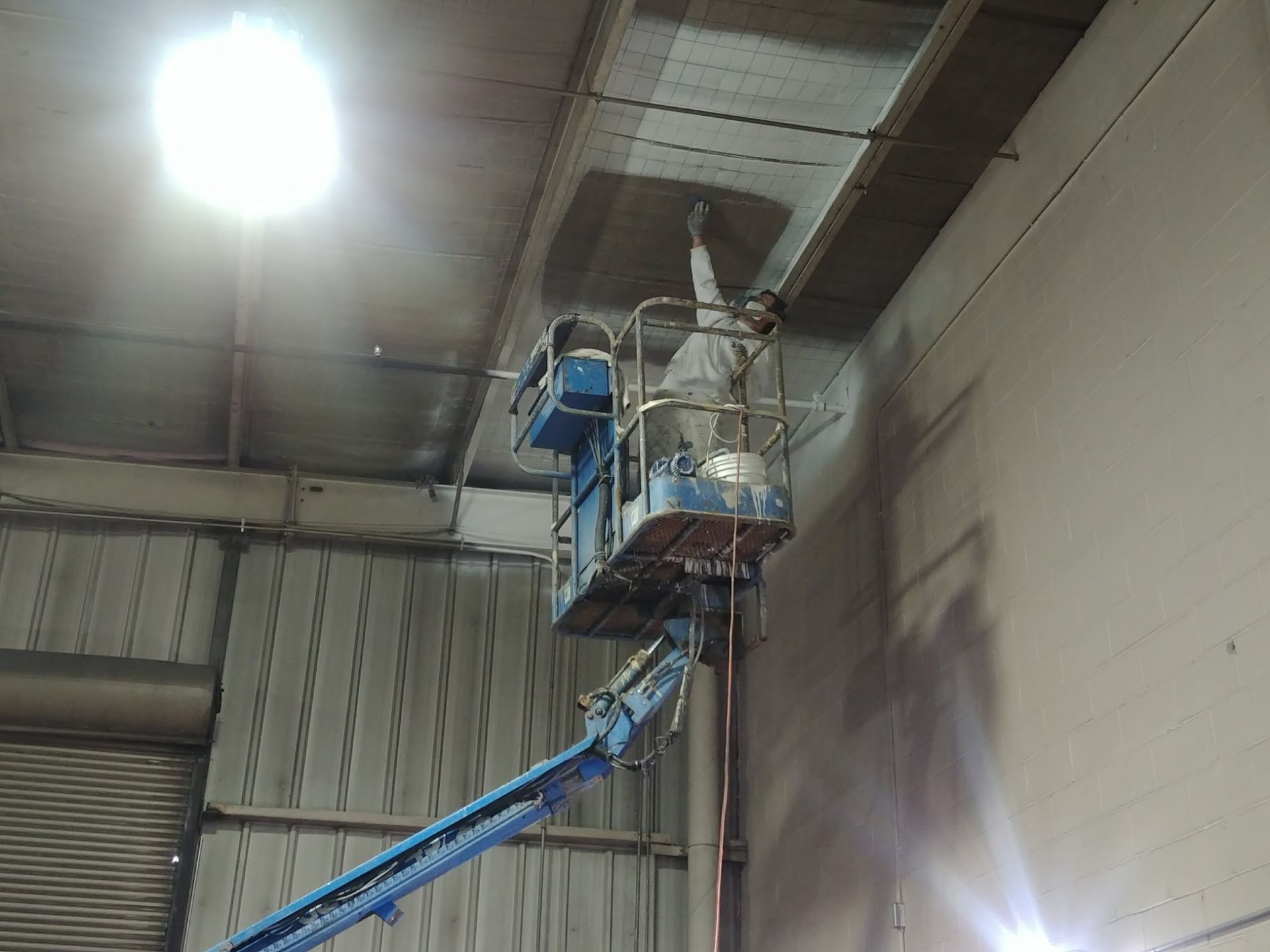 Worker on a lift repairing industrial ceiling ducting in a warehouse.